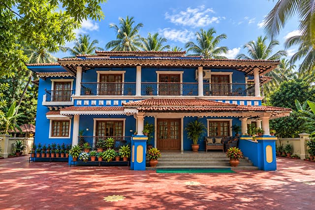 Misquita Exclusive Homestay in Benaulim, a blue two-storey Goan house with a shared porch and a red-oxide courtyard.