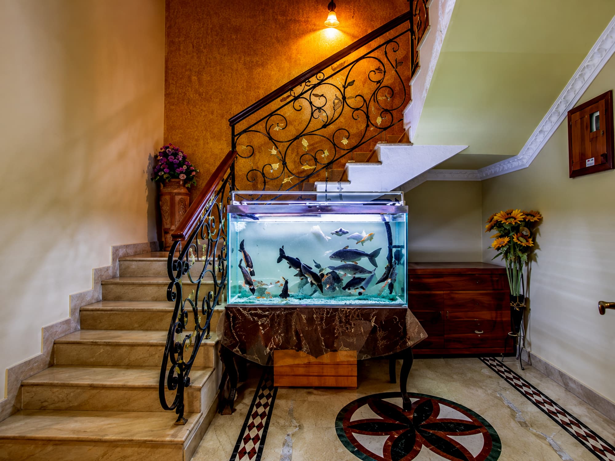 The marble staircase at Misquita Exclusive with a wrought-iron railing and a large aquarium.